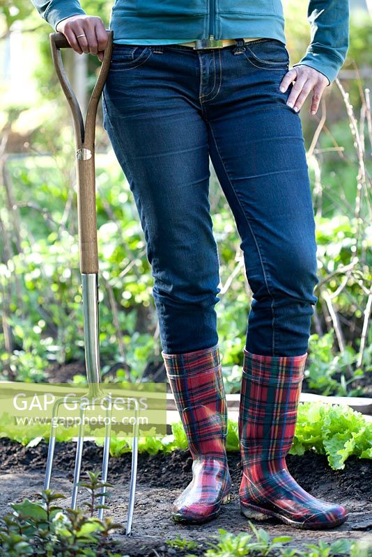 Woman in red wellies with stainless garden fork standing in the garden.