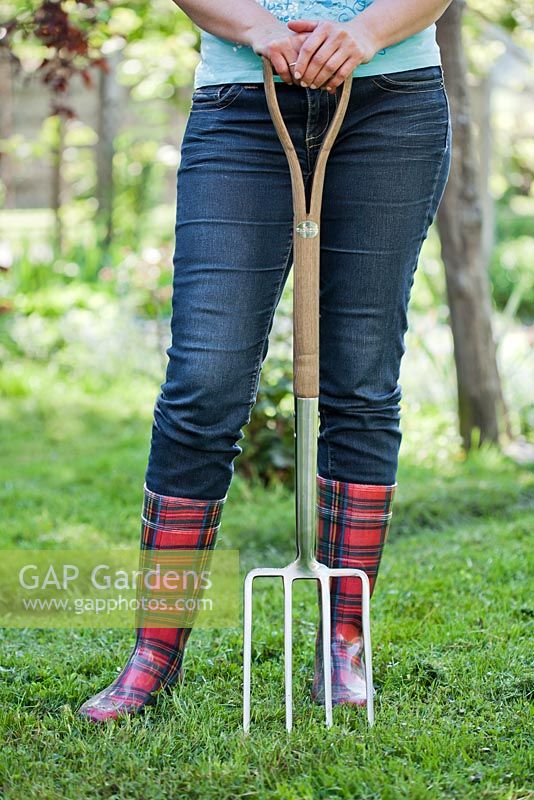 Woman in red wellies with stainless garden fork standing in the garden.