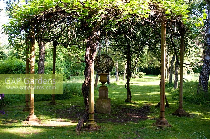 Sculpture sheltered under a gazebo in the woodland garden. Marle Place