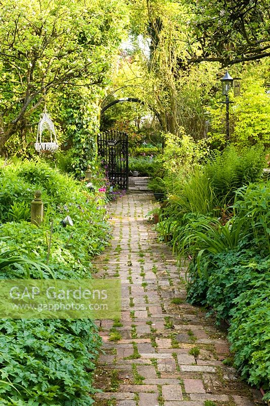 Brick pathway leading from walled orchard garden through gated arch towards the formal lawn - The Ridges, Chorley