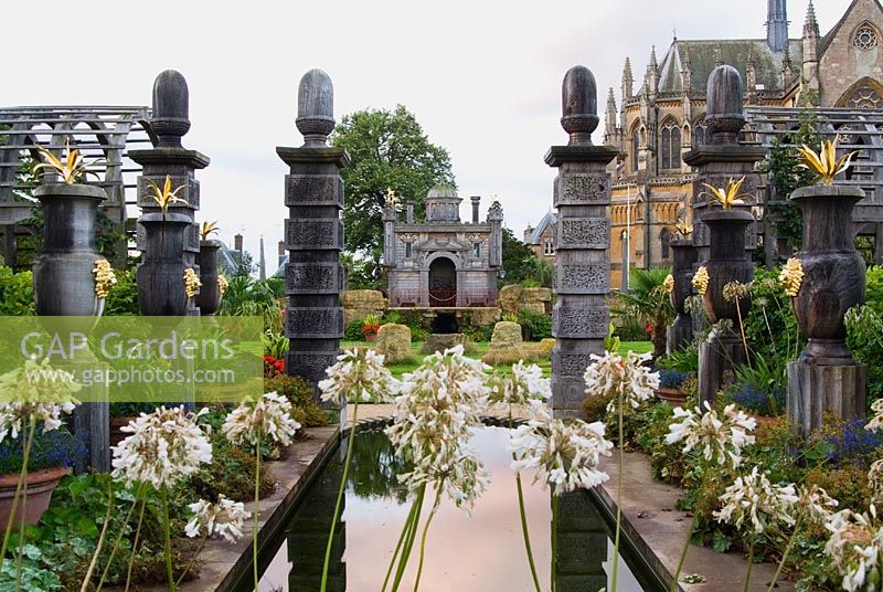 Rill pool flanked by turned oak urns spouting water, with gilded agaves in their tops. Oak columns with stylized acorns on the top frame a view of Oberon's Palace beyond. The Collector Earl's Garden designed by Julian and Isabel Bannerman.