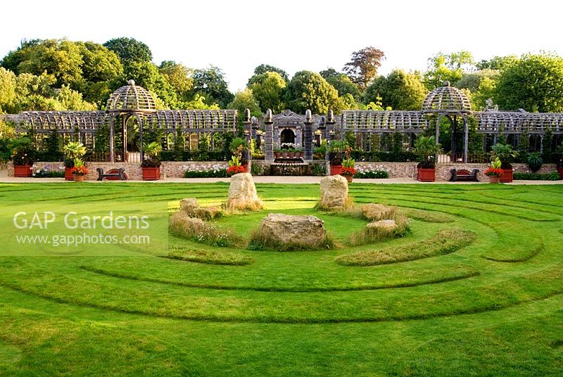 Double domed pergola in oak spans the garden dividing upper gravelled courtyards from the lower lawn featuring maze and central stones. The Collector Earl's Garden designed by Julian and Isabel Bannerman.