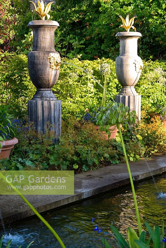 Rill pool flanked by turned oak urns spouting water through gilded lions' heads, with golden agaves in their tops. The Collector Earl's Garden designed by Julian and Isabel Bannerman.