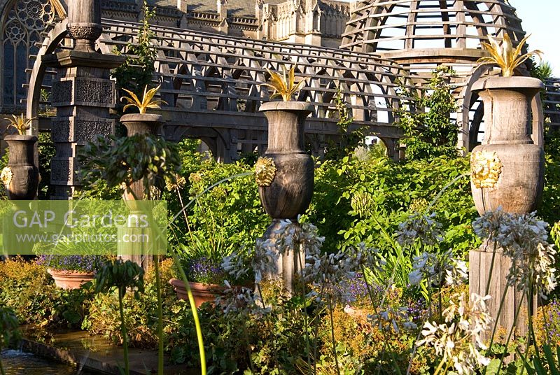 Rill pool flanked by turned oak urns spouting water through gilded lions' heads, with golden agaves in their tops. Oak columns with stylized acorns on the top and domed pergola frame a view of Arundel Cathedral beyond. The Collector Earl's Garden designed by Julian and Isabel Bannerman.