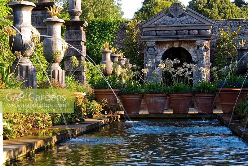 The allegorical River Arun emerges from a rocky grotto framed by a scallop shell pediment and muscular caryatids. It flows along a rill pool flanked by turned oak urns spouting water through gilded lions' heads, with golden agaves in their tops. The Collector Earl's Garden designed by Julian and Isabel Bannerman.