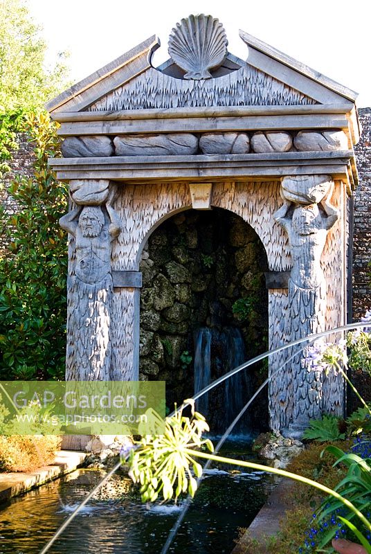 The allegorical River Arun emerges from a rocky grotto framed by a scallop shell pediment and muscular caryatids. It flows along a rill pool flanked by turned oak urns spouting water through gilded lions' heads, with golden agaves in their tops. The Collector Earl's Garden designed by Julian and Isabel Bannerman. 