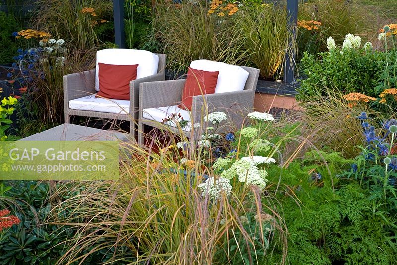 Modern wicker furniture on patio surrounded by Eryngium, Achilleas and grasses - 'The Landform Garden' - Gold medal winner and Best Summer Garden - RHS Hampton Court Flower Show 2012 