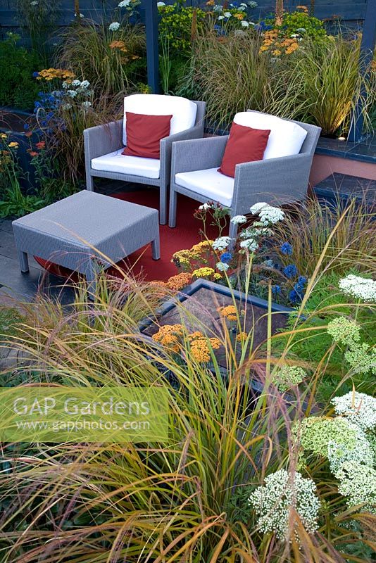 Modern wicker furniture on patio surrounded by Eryngium, Achilleas and grasses - 'The Landform Garden' - Gold medal winner and Best Summer Garden - RHS Hampton Court Flower Show 2012 
