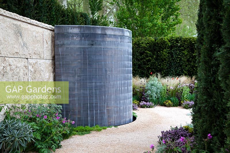 Curved water cascade on stone wall with gravel pathway softened by mediterranean-style planting.  