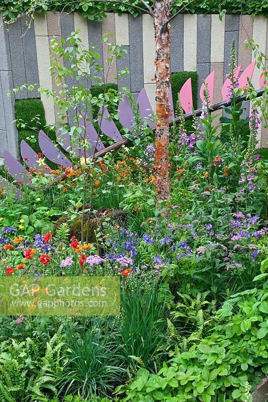 Colourful bladed curved sculpture and wall underplanted with perennials, ferns and grasses 