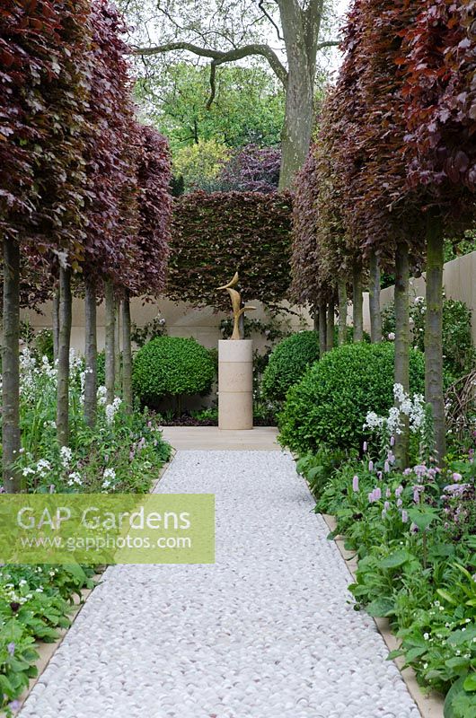 Cobblestone path leading to Bronze Bird sculpture by the late Breon O'Casey with pleached Fagus sylvatica 'Atropunicea' - The Laurent-Perrier Garden