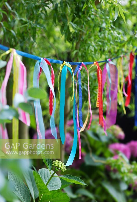 Home made garden bunting made from lengths of colourful ribbons knotted on to a length of ribbon