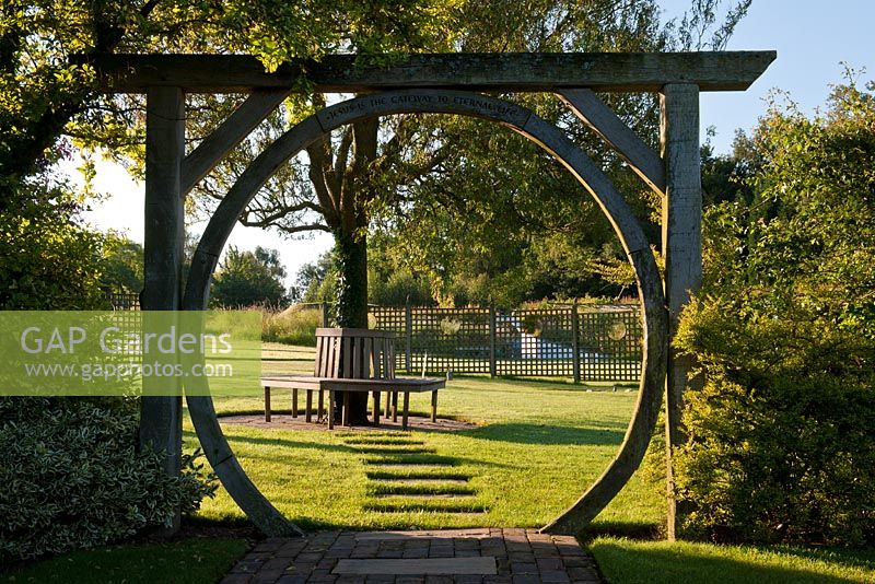 View through circular gate circlular view beech seat round tree focal point lawn summer July sun sunny Latchetts Sussex child friendly childrens garden plant combinations