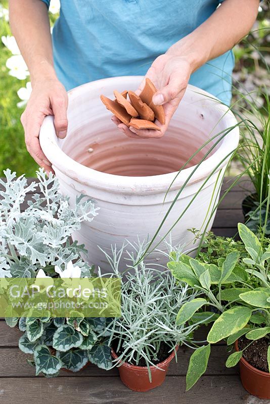 Step by step for planting silver and grey themed container - adding broken pieces of pot to aid drainage