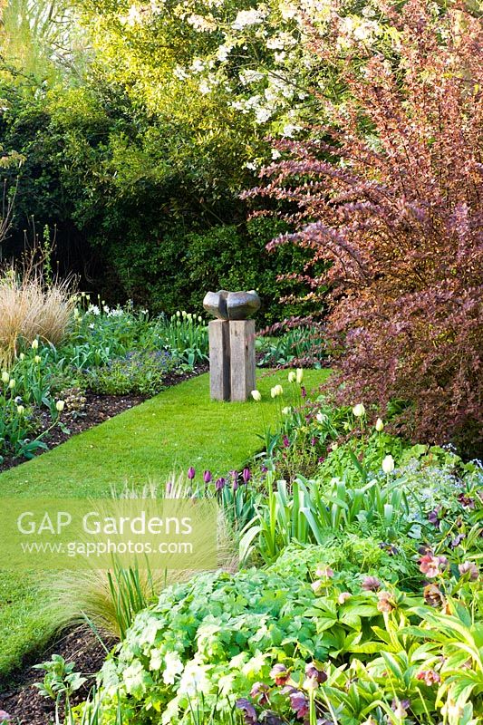 Modern sculpture and Spring border with Tulipa 'Recreado' and 'Spring Green'. Other plants include Stipa, Hellebores and Narcissus 'Thalia'
