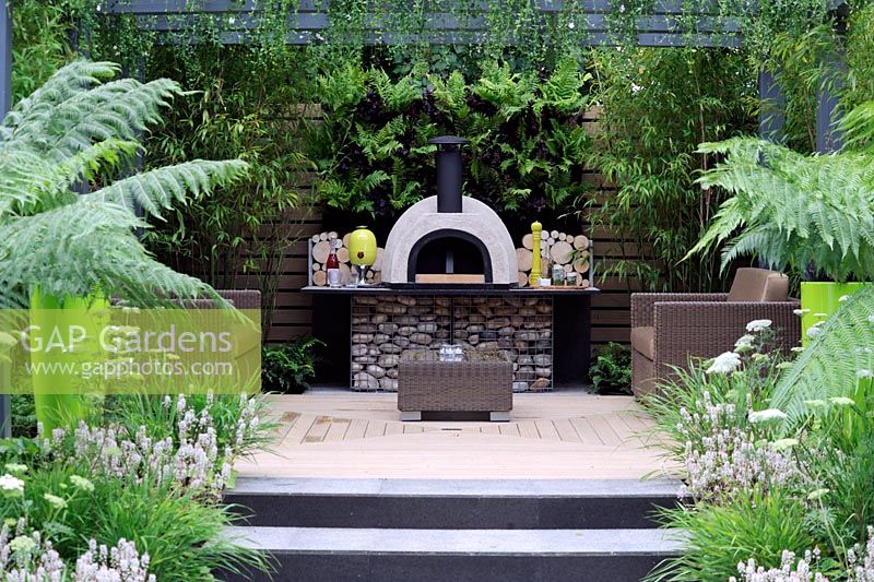 Outdoor living cooking area with wood burning oven and back wall planted with ferns and bamboo. Live Outdoors. Hampton Court Palace flower show 2012.