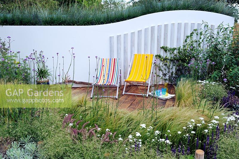 Extensive planting of grasses around timber decked patio area and above the curving back wall, 'Coastal drift garden', Hampton Court Palace Flower Show 2012
