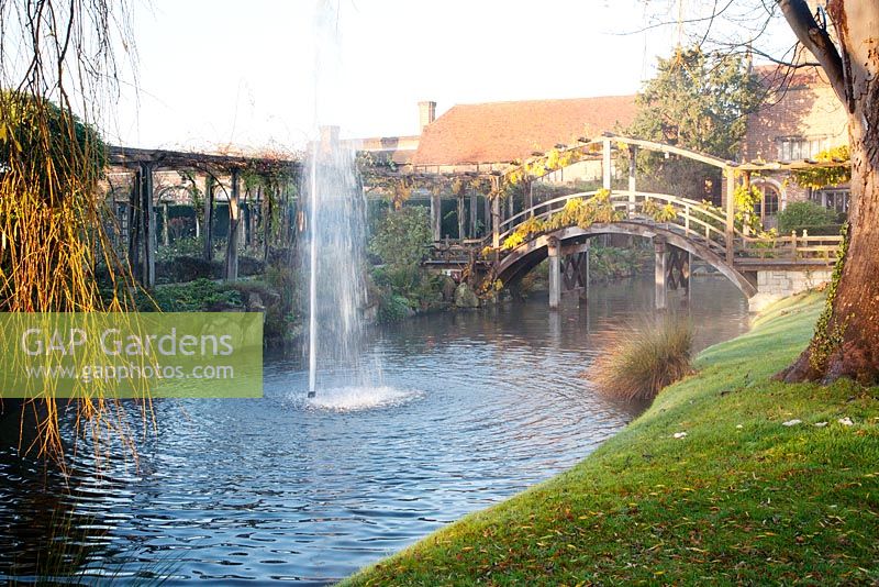 Wooden bridge over moat with fountain at dawn in winter - Great Fosters, Surrey 