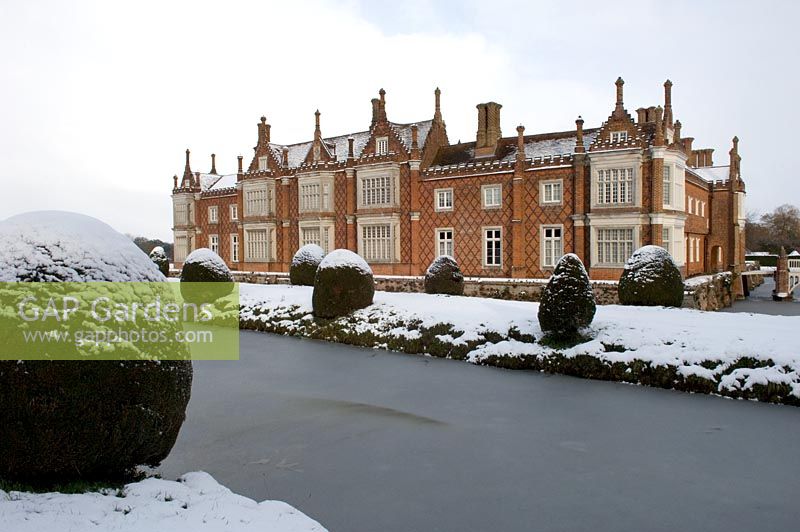 Frozen moat surrounding grand country house. Yew topiary in rows along banks