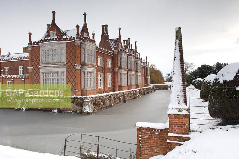Large country house covered in snow in winter surrounded by frozen frosty moat. 