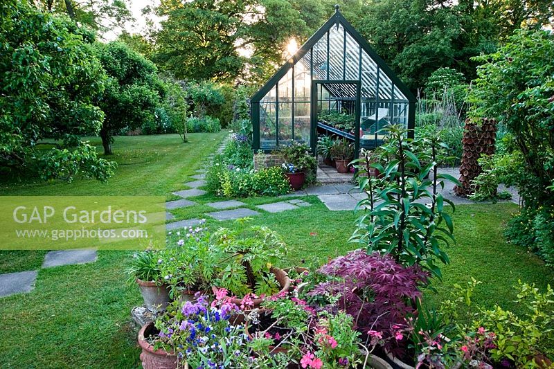 Sun rising behind greenhouse with simple slab path through lawn and collection of terracotta pots in foreground. Beechenwood Farm, Odiham, Hants, UK