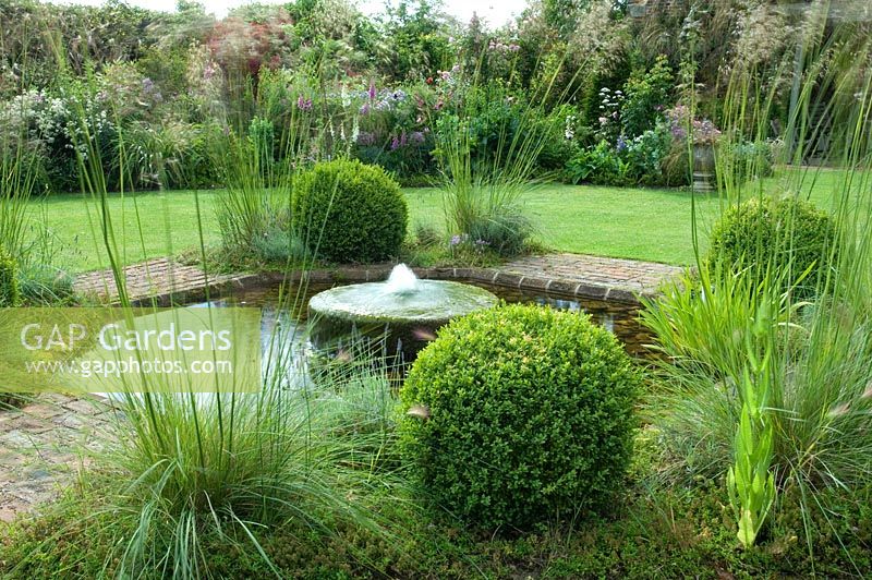 Millstone fountain surrounded by Buxus spheres and Stipa gigantea
