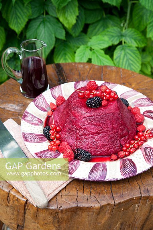 Summer Pudding decorated with fruit and coulis made by Lesley Wild on wood table in the garden.