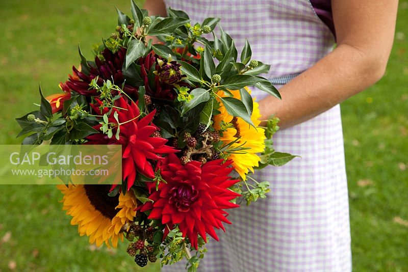 Large Autumnal multicoloured handtied bouquet with Sunflowers, Dahlias, Blackberries and Ivy foliage, held by Georgia Miles of The Sussex Flower School.