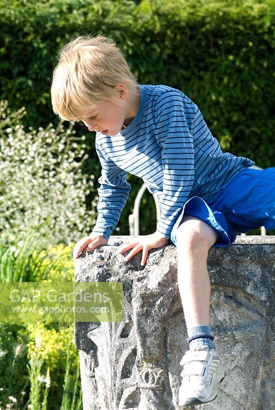 Boy on the old stone well head in The White Garden, Wood Farm. June