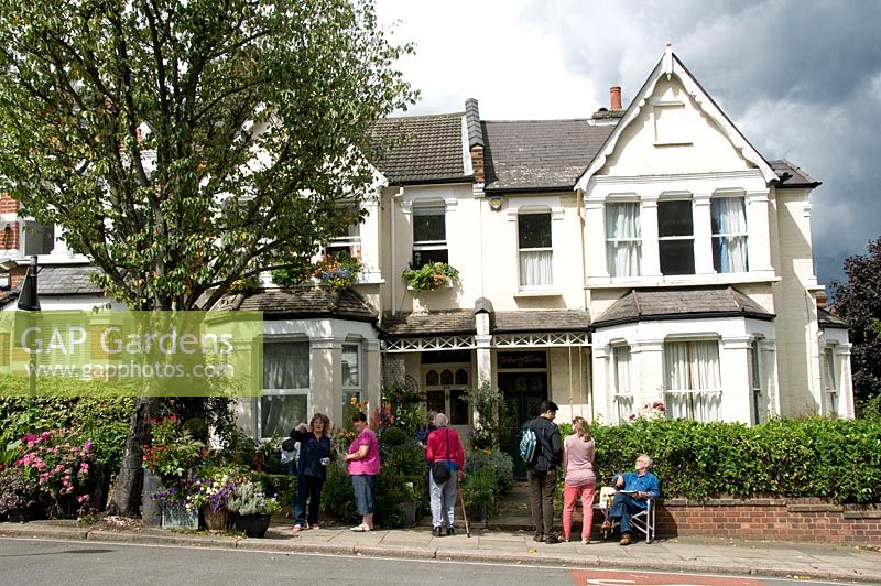 People talking in front suburban garden open under the National Garden Scheme NGS, plants in large pots edge the pavement - Alexandra Park Road Gardens Group, London Borough of Haringey