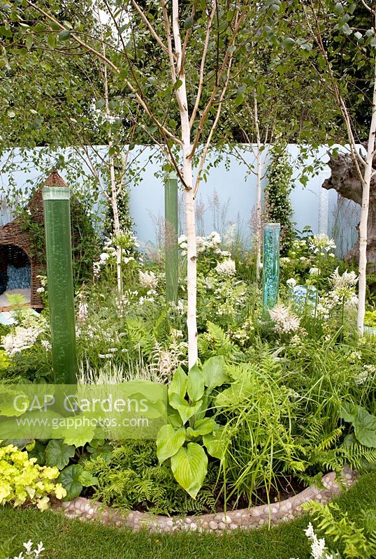 Bubbling water tubes amongst ferns, Hostas, Astilbe, grasses and Betula with willow playhouse - 'A corner of the world garden', RHS Hampton Court Palace Flower show 2012