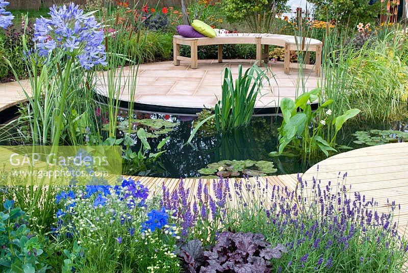 Central pond, surrounded by a decked path that leads to a seating area with sandstone paving and planting of Agapanthus, Cerinthe, Lavandula, Heuchera and Delphinium. 'A Taste of Ness' garden sponsored by Friends of Ness Gardens and designed by Phillippa Probert. RHS Tatton Flower Show 2012