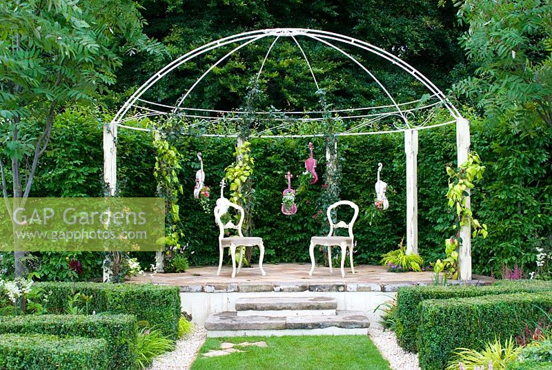 Domed secluded pergola covered in climbers, painted violins and cellos overgrown with plants and Buxus topiary hedges in the 'Air on a Green String' garden - RHS Tatton Flower Show 2012