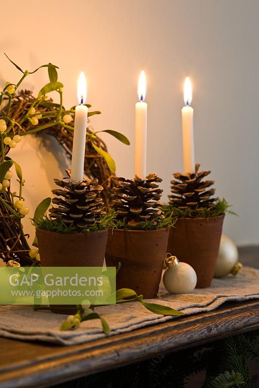 Candles with terracotta holders decorated with fir cones and moss