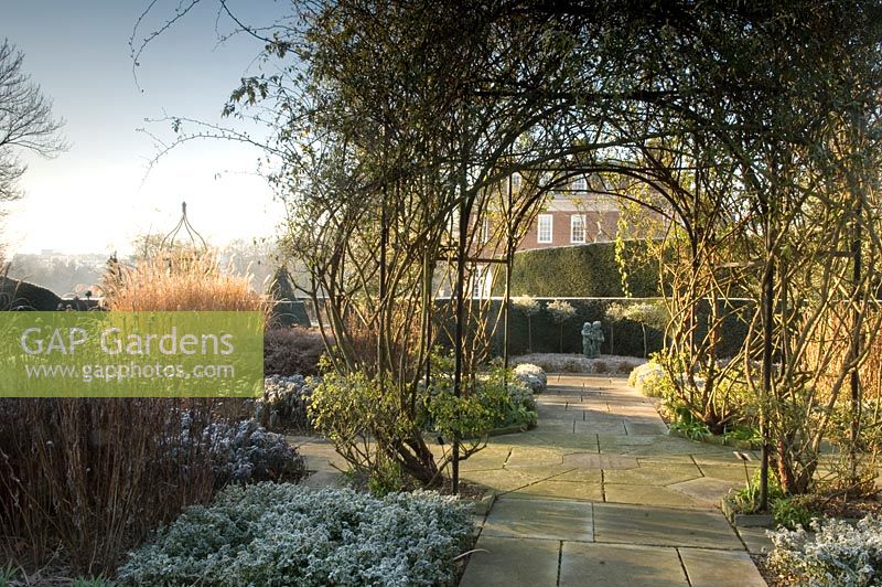 Winter formal garden with Rosa growing over arch and yorkstone paving - Winfield House
