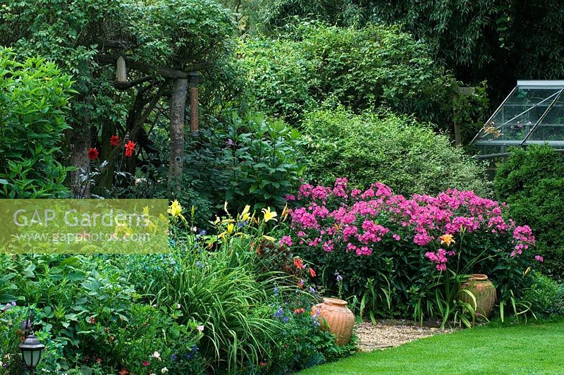 Wildlife conservation garden with borders of Hemerocallis, Phlox, Cerinthe and Dahlia flanking rustic arch 