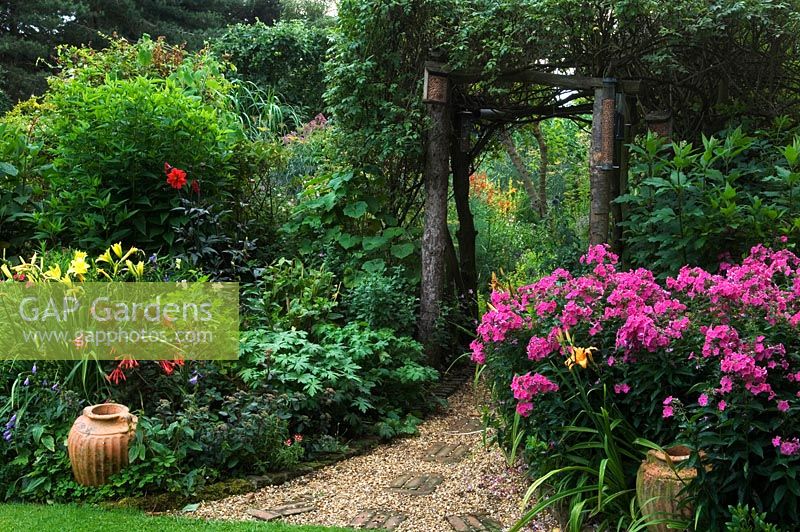 Wildlife conservation garden with arch over brick and gravel path and border of Dahlia, Phlox and Hemerocallis 