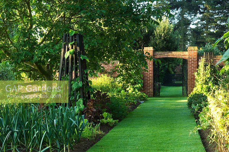 Wildlife conservation garden with long mown grass path, obelisk, brick arch and metal gates