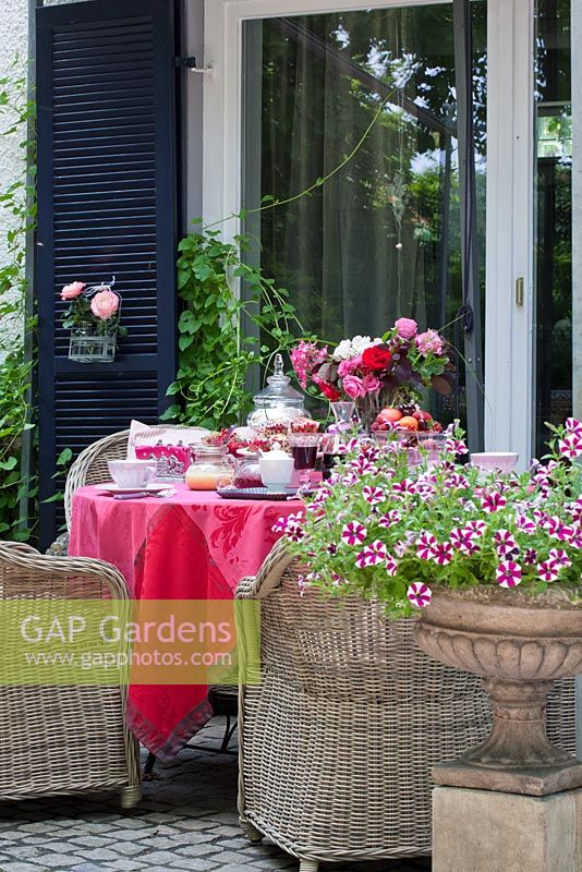 Terrace with Petunia in a metal urn in front of red linen clothed table prepared for breakfast.
