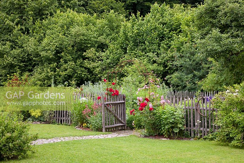 A garden within the garden. A granite paved path goes to the entrance of a traditional German country garden with wooden picket fence. A free growing hedge of native shrubs including Centranthus ruber 'Coccineus', Roses and Currants