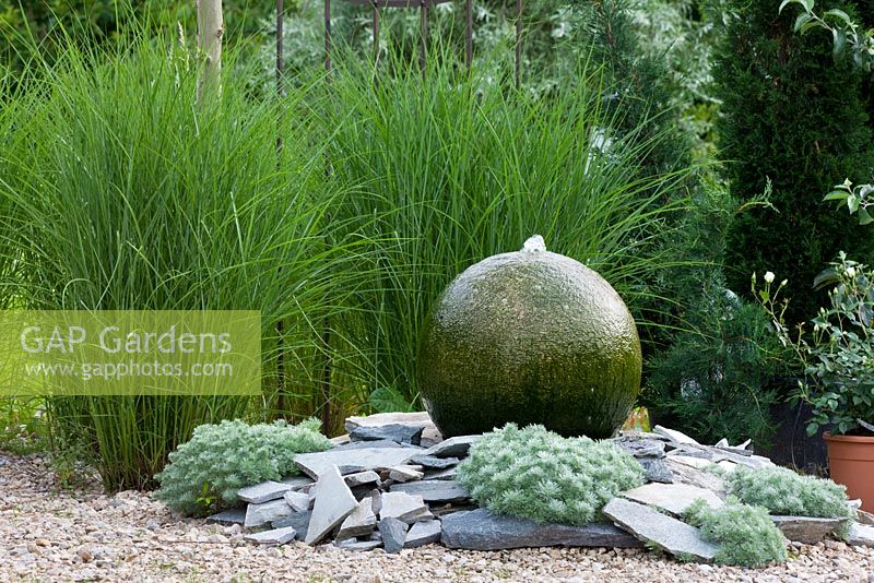 Backed by a Miscanthus group, water feature of granite sphere and shingles planted with Artemisia schmidtiana 'Nana' and Miscanthus sinensis