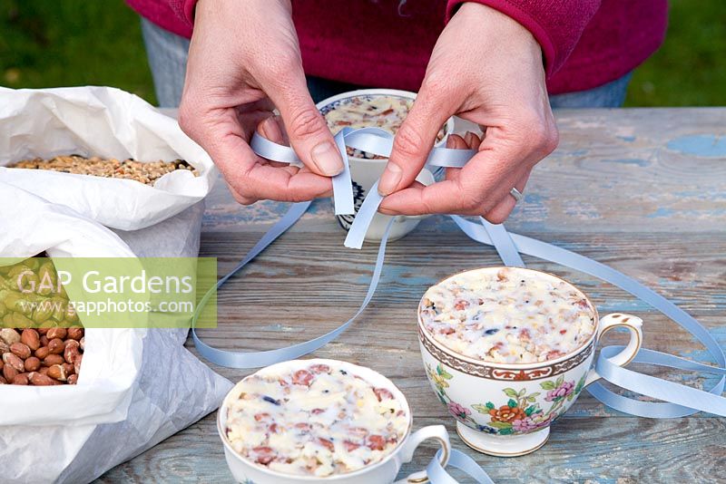 Step by step for creating hanging bird feeders out of teacups and yoghurt pots - tying on ribbons to suspend 