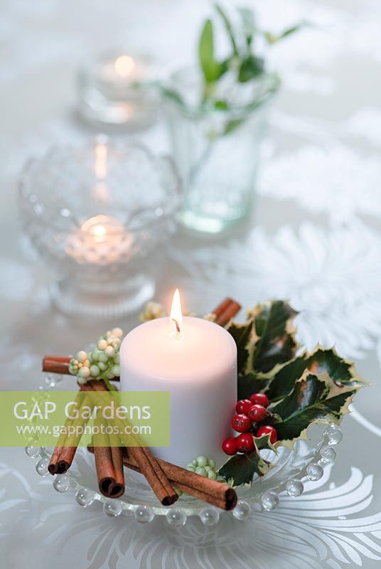 Table candle decoration with holly, red berries and cinnamon sticks