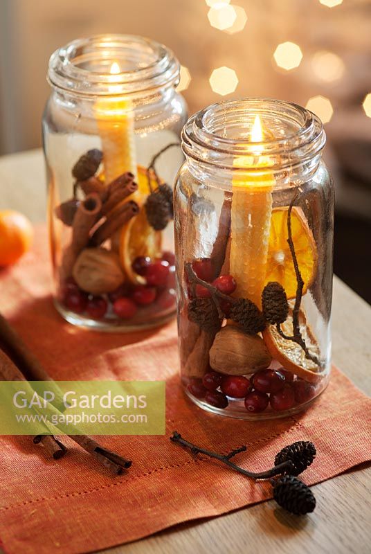 Old glass jars filled with cranberries, cinnamon sticks, dried orange slices, walnuts and larch cones with beeswax candles