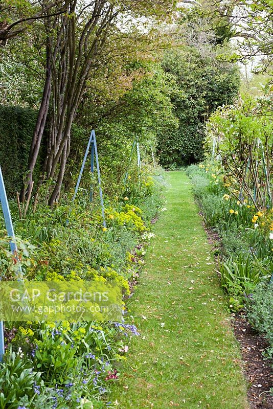 Row of decorative obelisks amongst spring planting - West Green House, Hampshire