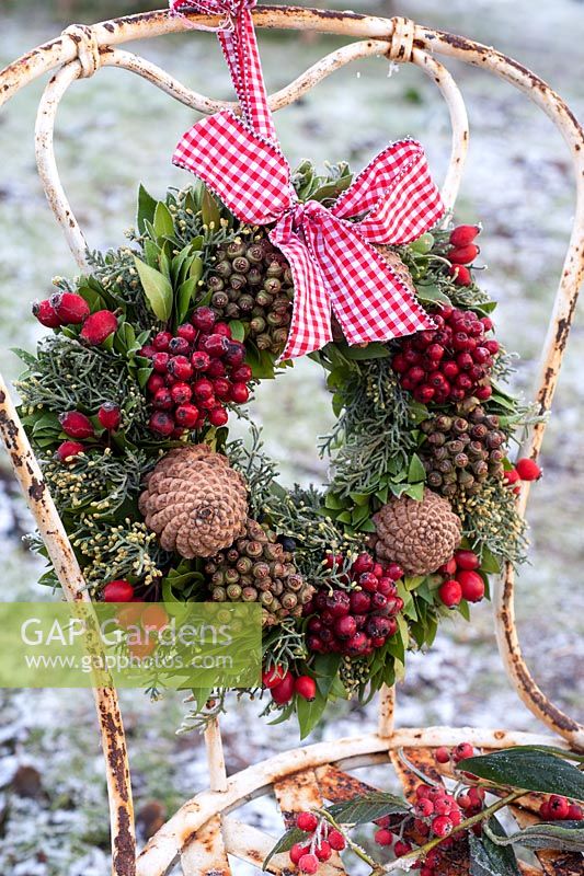 Frosted wreath with berries and cones tied with ribbon to old metal chair