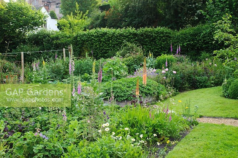 View of carefully managed country garden with flower filled borders merging in to vegetable garden with raised beds