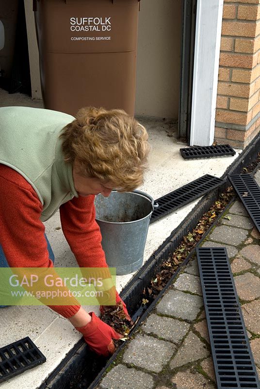Woman clearing fallen dead leaves from guttering channel at garage entrance