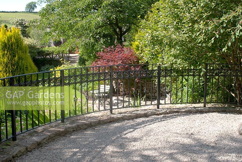 Raised gravel area with ornamental railings overlooking mature garden with trees and conifers. The garden is open for the National Garden Scheme in Dalton Hamlet, Cumbria.