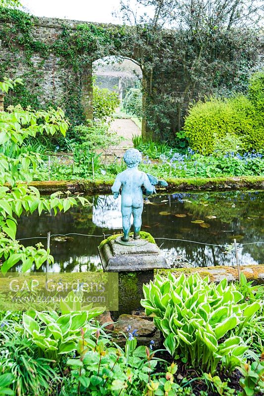 Pond garden planted with acers, ferns and hostas around a formal pool, with putto. Wayford Manor, Wayford, Crewkerne, Somerset, UK